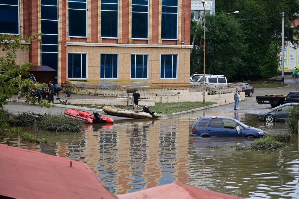 Pedestrians walk next to a flooded road in the Russian far-eastern city of Ussuriysk on Aug 14, 2023. - (Photo by PAVEL KOROLYOV / AFP)