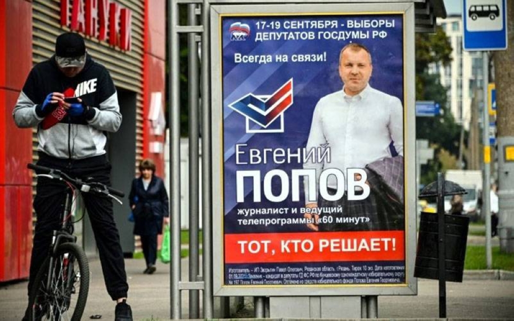 Gambar fail menunjukkan seorang penunggang basikal menggunakan telefon bimbit di sebelah poster kempen pilihan raya parlimen di Moscow. - Foto AFP