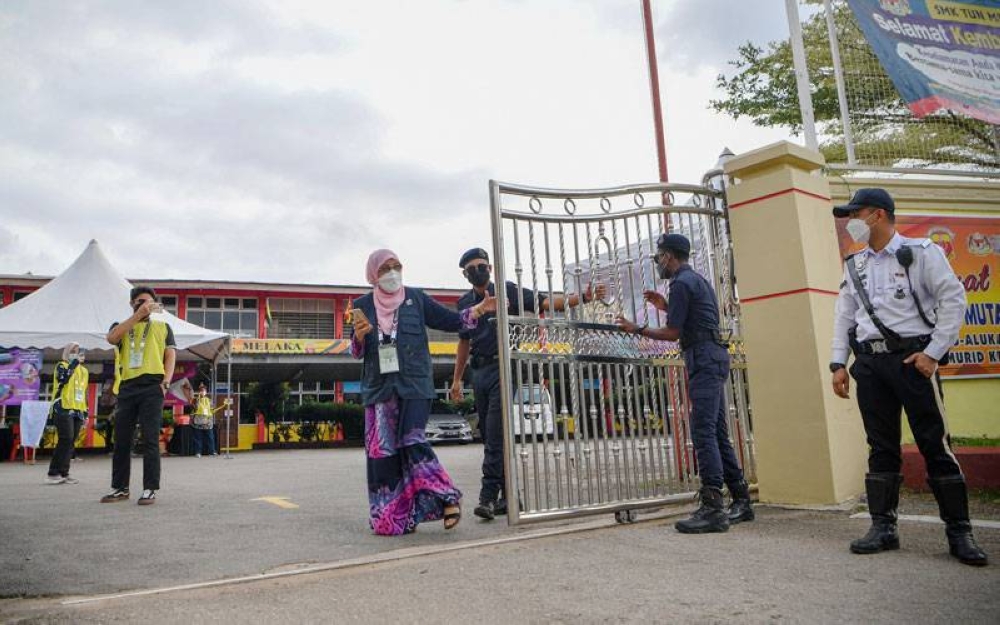 Penyelia Pusat Pembuangan Undi Sekolah Menengah Kebangsaan Tun Mutahir, Darma Taksiah Kamaruddin (tengah) bersama anggota polis menutup pagar utama tepat jam 5.30 petang selepas waktu pengundian PRN Melaka tamat di Batu Berendam pada Sabtu.