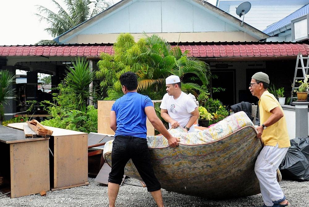 Buang Abdul Basir, 67, (kanan) dibantu anak-anaknya mengeluarkan perabot dan perkakas rumah yang rosak di Kampung Jalan Kebun Seksyen 30 Shah Alam pada Ahad.