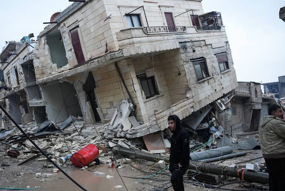 Seorang penduduk berdiri di depan bangunan runtuh akibat gempa bumi berlaku di bandar Jandaris di wilayah Aleppo, Syria. - AFP