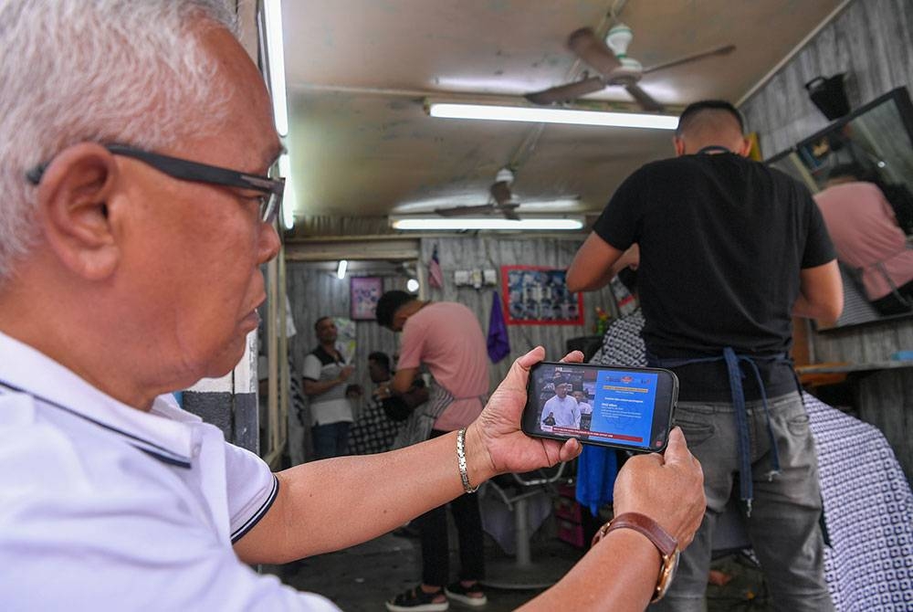 Orang ramai mendengar pembentangan Belanjawan 2023 Malaysia Madani disampaikan Perdana Menteri yang juga Menteri Kewangan, Datuk Seri Anwar Ibrahim melalui telefon pintar di kedai gunting rambut sekitar Kuala Lumpur pada tinjauan pada Jumaat. - Foto Bernama