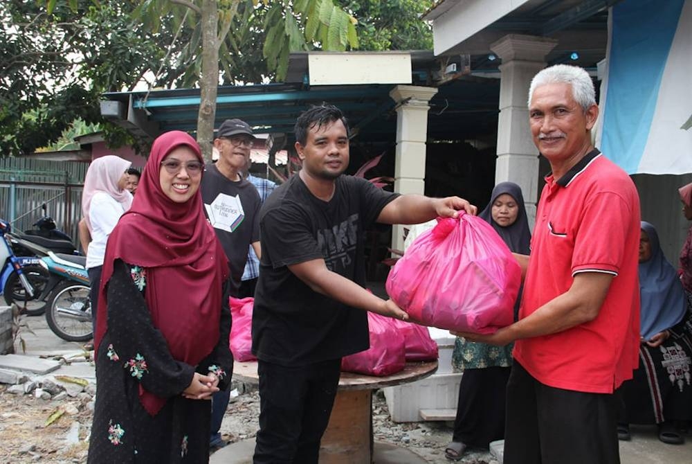 Siti Mastura (kiri) menyerahkan sumbangan barang makanan semasa menjayakan program jualan ikan murah di Kubang Menerong pada bulan Ramadan.