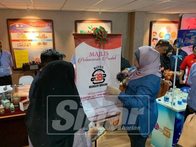 Rina memotong riben pelancaran produk Burger Bakar ketika lawatan ke KIM di Pengkalan Chepa, hari ini.
