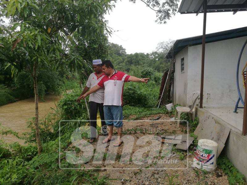 Mohd Nazry (depan) dan Omar menunjukkan tebing runtuhan semakin hampir dengan rumah penduduk
