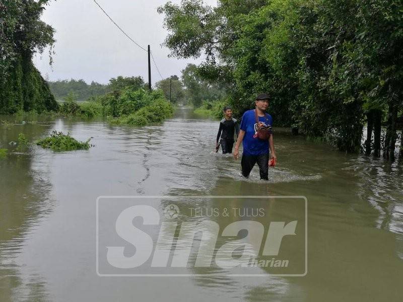 Nik Zamari bersama anaknya mengharung air sejauh 3km untuk keluar membeli barang dapur selepas jalan utama di Kampung Kubang Pak Itam, Meranti di sini ditenggelami banjir.