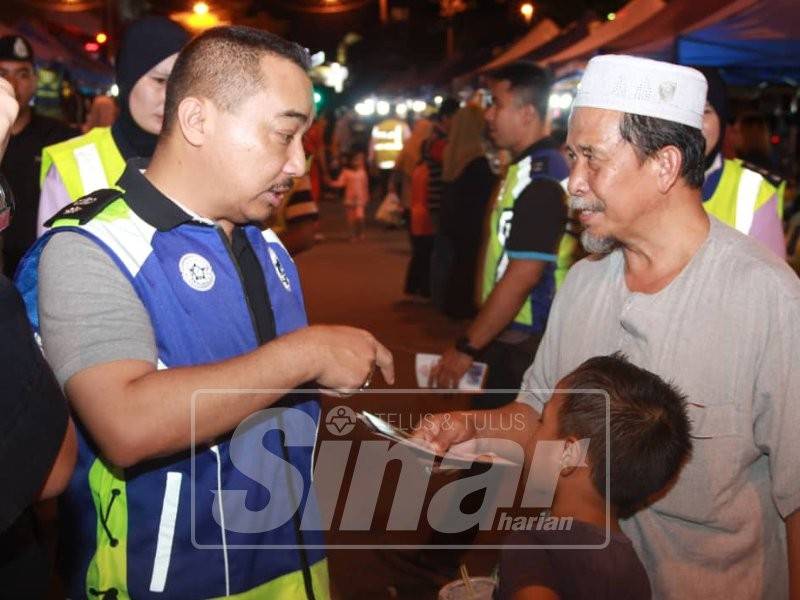 Suffian (kiri) sedang memberi penerangan tentang kesedaran jenayah kepada salah seorang pengunjung KT Walk, Jalan Sultan Ismail, di sini, malam tadi.