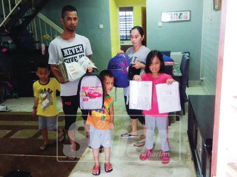 Ahmad Razif bersama isteri dan anaknya menunjukkan barangan sekolah yang basah dan rosak akibat banjir lumpur.
