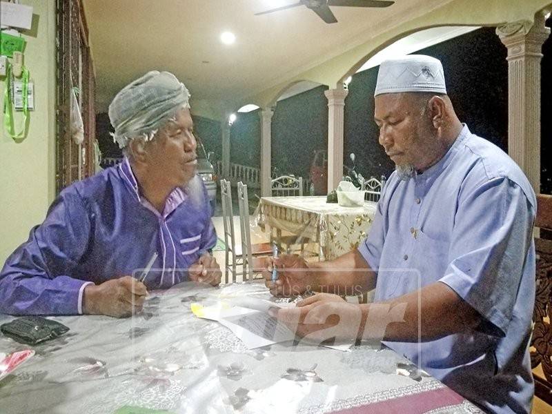 Ustaz Din (kanan) melayani penduduk kampung dalam urusan berkaitan