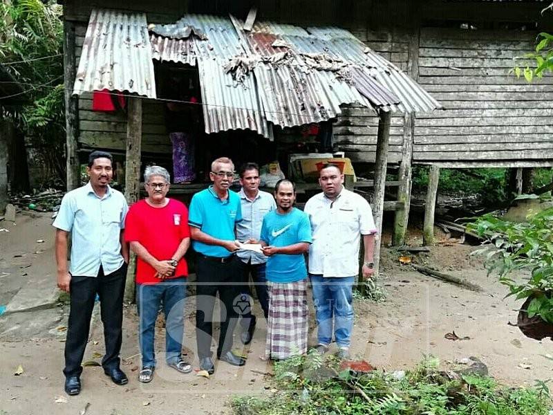 Nor Asuki (dua, kanan) menerima sumbangan wang tunai dan barangan keperluan harian daripada Mohd Rafi di hadapan rumahnya di Kampung Lubuk Bongor.