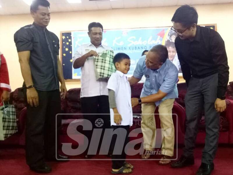 Amiruddin memakaikan baju sekolah kepada salah seorang penerima bantuan dalam Parlimen Kubang Pasu, hari ini.