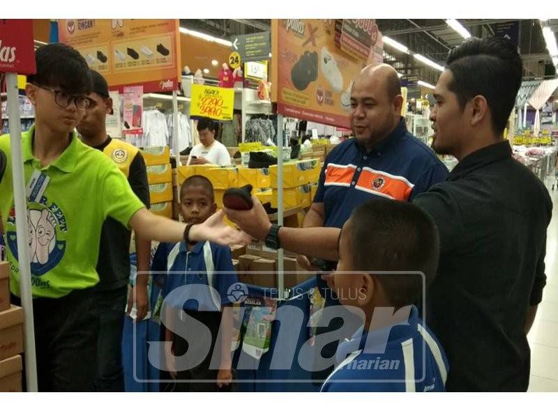 Hasnul Fairuz (dua, kanan) melayani anak-anak yatim memilih kasut sekolah di Pasar raya Besar Mydin Meru, di sini.