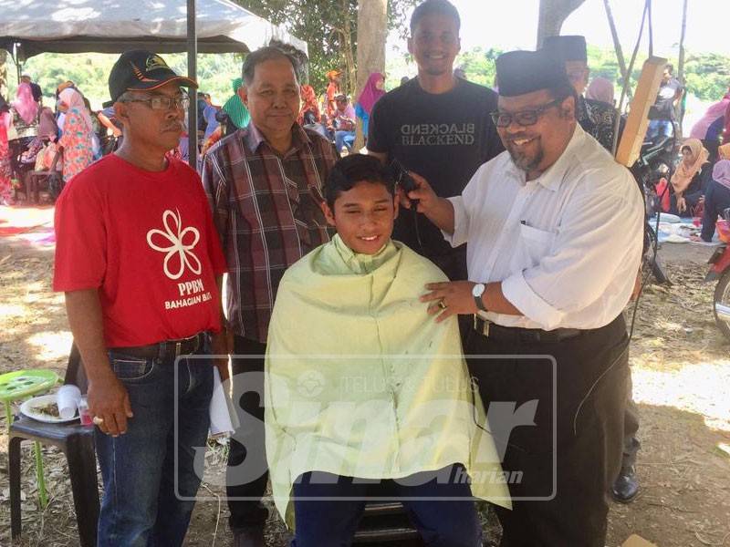 Tarmizi (kanan) sempat mencuba memotong rambut salah seorang kanak-kanak pada program kenduri kampung, di sini, baru-baru ini.