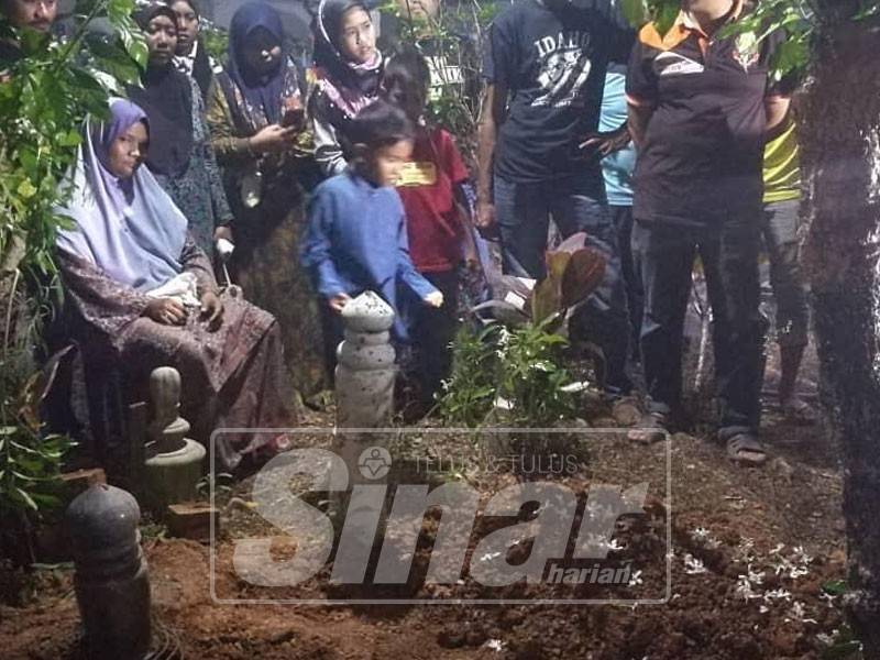 Ibu mangsa, Norhasyelawati (duduk) melihat majlis pengebumian dua anaknya sambil memangku anak sulong beliau, Muhamad Hakim, 7.