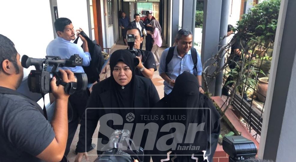 Tertuduh (kanan) berpurdah keluar dari mahkamah dikawal anggota SPRM selepas tidak mengaku ke atas semua tuduhan itu.