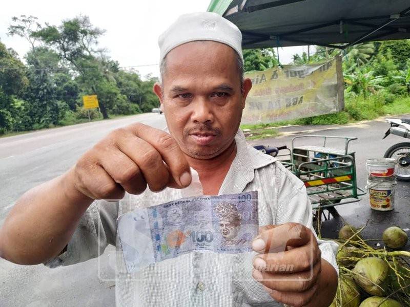 Jaafar menunjukkan sekeping wang palsu bernilai RM100 daripada pelanggannya yang membeli dua gelas air kelapa.