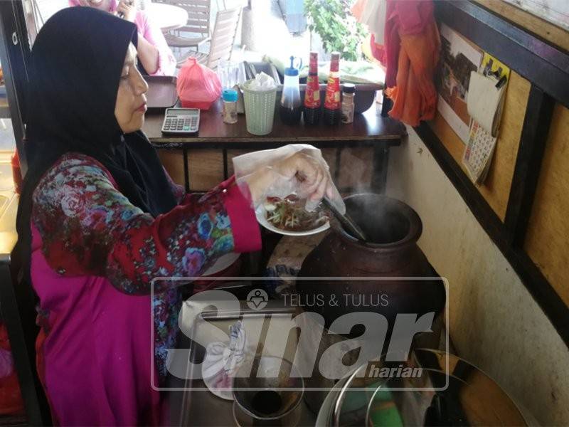 Salasiah menyediakan kuah laksa yang dimasak dalam buyung tanah liat.