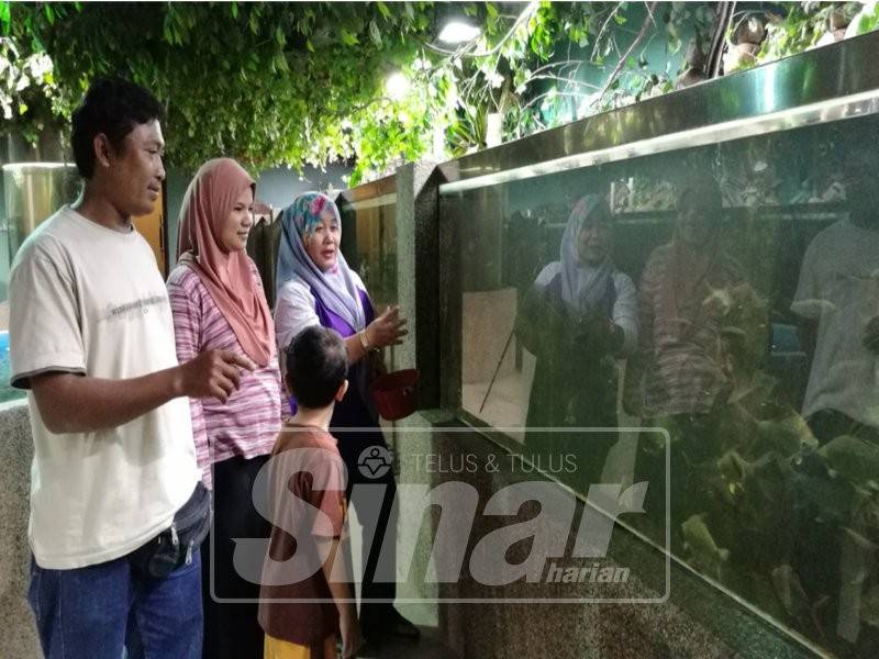 Melah (kanan) memberi penjelasan kepada pengunjung bahagian akuarium Pusat Penerangan Kenyir, di Pengkalan Gawi, Tasik Kenyir. 