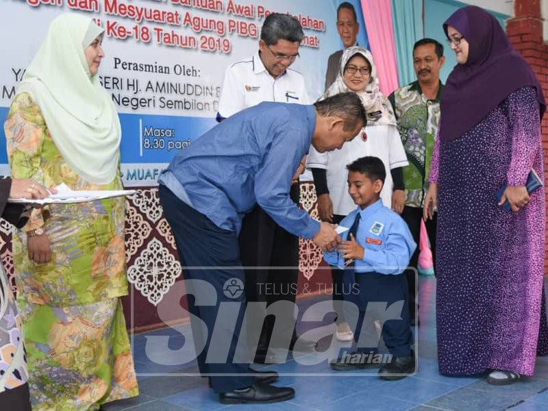 Aminuddin menyampaikan sumbangan awal persekolahan kepada salah seorang murid di SK Sikamat, semalam.
