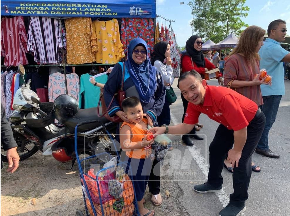 Maszlee (kanan) mengedarkan limau kepada pengunjung Pasar Jumaat di Simpang Renggam.