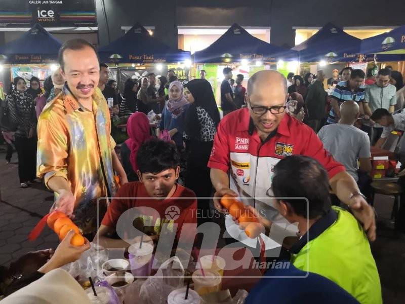 Hisyamuddin (kiri) bersama Ariffin (kanan) mengagihkan limau kepada pengunjung di Medan Warisan Makanan Dataran Bandaraya Kota Bharu malam ini.