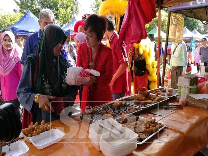 Nicole Tan menyampaikan sumbangan kepada pengunjung di Pasar Tani Paroi Jaya, semalam.
