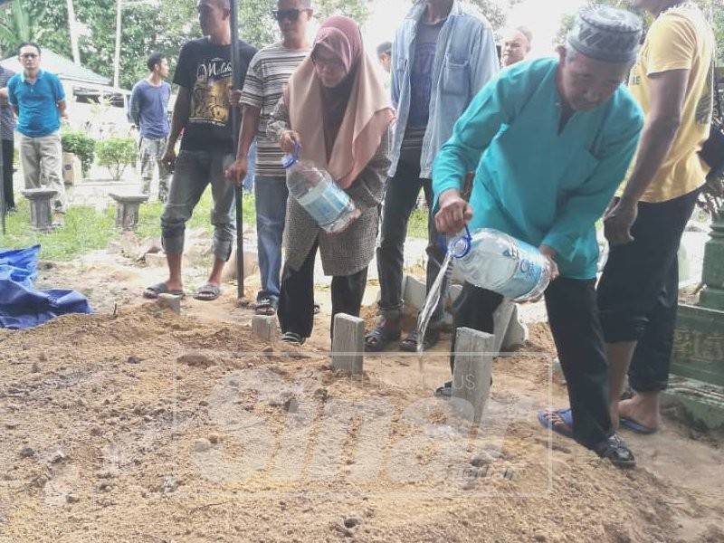 Januri (kanan) bersama Rusinah (tengah) menyiram air di pusara anak, menantu serta dua cucunya di Tanah Perkuburan Islam Kampung Bentong Dalam, Kluang.