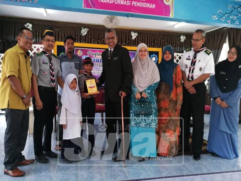 Mohamed Hanipa menyampaikan anugerah Unsung Hero kepada murid SK Putera Jaya, Muhamad Hisham Ismail, 11, hari ini.