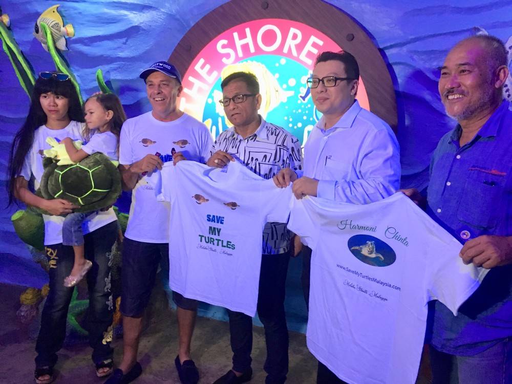 Norizam (tengah) dan Fong (dua, kanan) menerima baju T kempen kesedaran selamatkan penyu di Program Konservasi Penyu di The Shore Oceanarium Melaka, semalam. Turut kelihatan, Harmoni bersama ibu dan bapanya iaitu Luke Adam dan Farhana. 