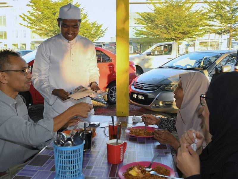 Calon Pakatan Harapan (PH) N24 Semenyih, Muhammad Aiman Zainali (dua, kiri) beramah mesra serta mengedarkan risalah kempen kepada penduduk setempat kertika sarapan pagi di Warung Nasi Lemak Omak Den Batu 2, hari ini. Foto: Bernama