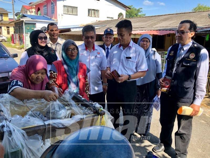 Zaini (dua, kanan) menyampaikan risalah kesihatan kepada penduduk di Wakaf Mek Zainab.