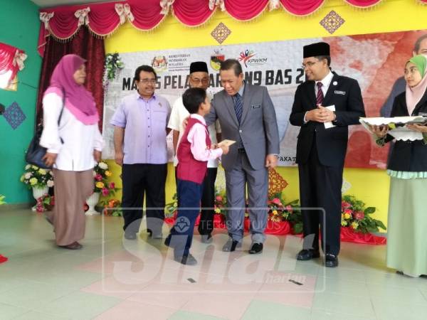 Aminuddin menyerahkan bantuan N9 Bas kepada murid terlibat.