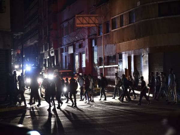 Orang ramai menyeberangi sebuah jalan di Caracas dalam keadaan gelap. - Foto AFP