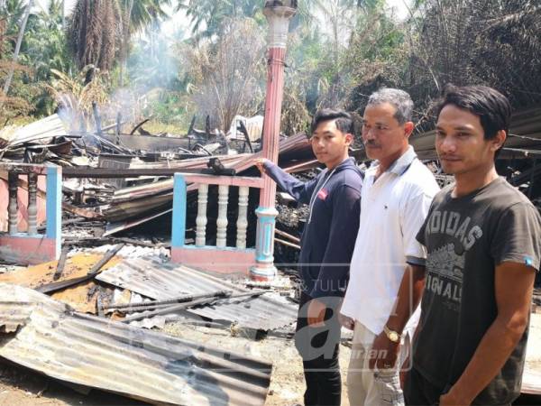 Muhammad Fahmi (kiri) bersama datuk dan bapa saudaranya menunjukkan keadaan rumah Sezali yang terbakar di Jalan Parit 1 Barat, di sini.