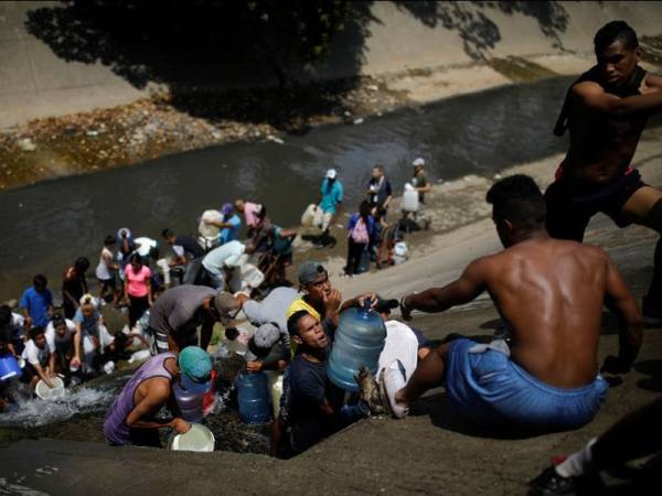 Penduduk di Venezuela menadah air yang dilepaskan melalui saluran kumbahan yang mengalir ke Sungai Guaire. - Foto Reuters