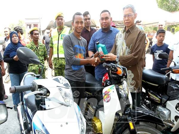 Mustapa (kanan) menyerahkan minyak hitam kepada salah seorang peserta Program Menukar Minyak Pelincir Motosikal di R&R Gemang, di sini, hari ini.