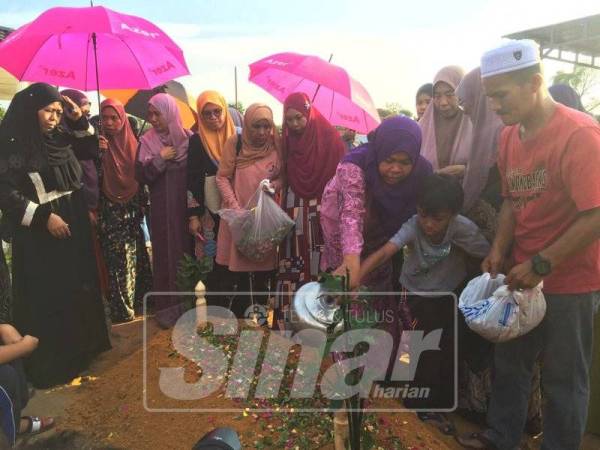 Nor Azawiah (tiga kanan) membantu anak lelakinya menyiram pusara arwah suaminya.