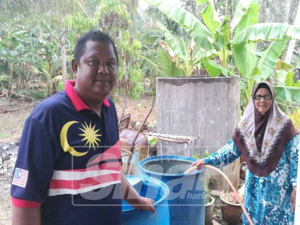  Asmadi (kiri) membantu Bechik menadah air bersih di dalam tong di rumahnya di Kampung Parit Makuaseng.