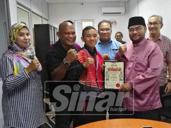 Mujahid (dua, kanan) menyerahkan sijil penghargaan dan sumbangan wang tunai kepada Mohammad Firdaus (tengah) yang bergelar juara dunia sukan Muay Thai sambil diiringi Khairunnizam (dua, kiri).