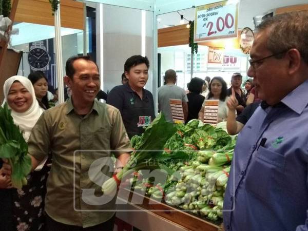 Abdul Yunus (dua, kanan) menunjukkan sayur yang dijual RM1 seikat pada sesi 'happy hour' sambil diperhatikan Zainal Abidin (kanan).