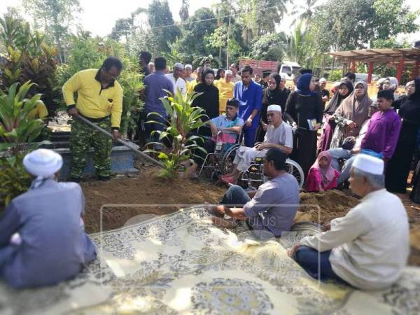 Mustafa (kerusi roda, tengah) dan Azmi (kerusi roda, kiri) menyaksikan upacara pengebumian ibu mereka, pagi tadi.