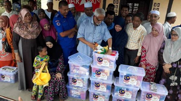 Mahfuz (tengah) menunjukkan barangan sumbangan keperluan yang diagihkan kepada 20 mangsa ribut di Parlimen Pokok Sena.