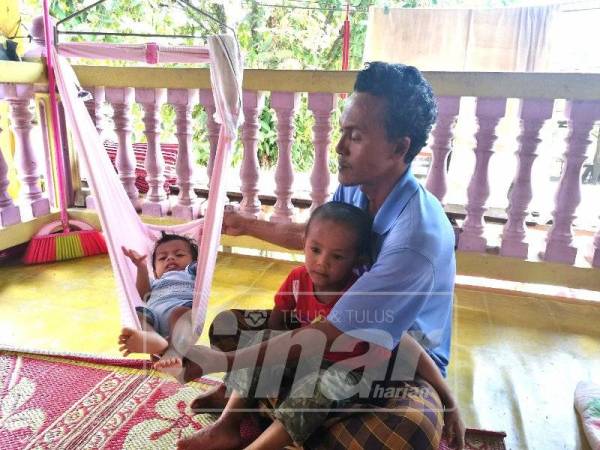 Che Sakri mendodoi anak bongsunya di dalam buaian sambil meriba anak keduanya.