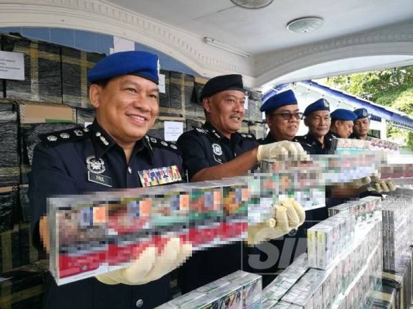 Paul (kiri) menunjukkan rokok seludup yang dirampas dalam serbuan awal pagi semalam.