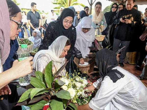 Balu Muhammad Arie Irawan Ahmaf Fauzi, Wan Edna Marina Wan Malik (dua, kiri) menabur bunga di atas pusara suaminya setelah jenazah selamat dikebumikan di Tanah Perkuburan Bukit Kiara hari ini. - Foto Bernama