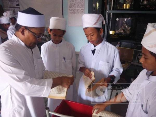 Fadzli (kiri) menunjukkan kaedah melupuskan al-Quran kepada pelajar Tahfiz Madrasah Tahfizul Quran al-Furqan. 