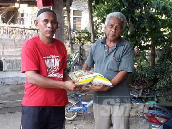 Mohd Zaki (kiri) menyampaikan sekampit beras kepada salah seorang penduduk Kampung Tebakang.