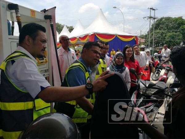 Saifuddin (tengah) membantu pengguna motosikal mengisi minyak di Stesen minyak Shell