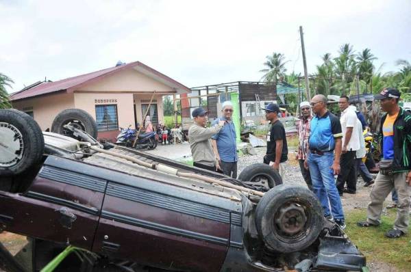 Abdul Yunus (kiri) meninjau keadaan ribut melanda rumah Rosnan (tiga dari kiri) dan menyebabkan kereta miliknya terbalik di Kampung Parit Mat Ali Tengah, Kuala Kurau, semalam.