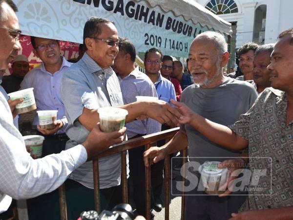 Dr Ahmad Samsuri (tengah) mengagihkan bubur lambuk kepada orang ramai di Masjid Abidin semalam.